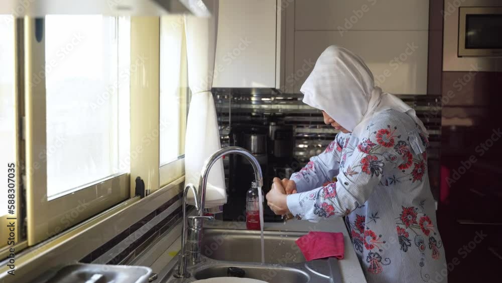 Middleaged muslim woman does housework Kitchen cleaning sink wearing