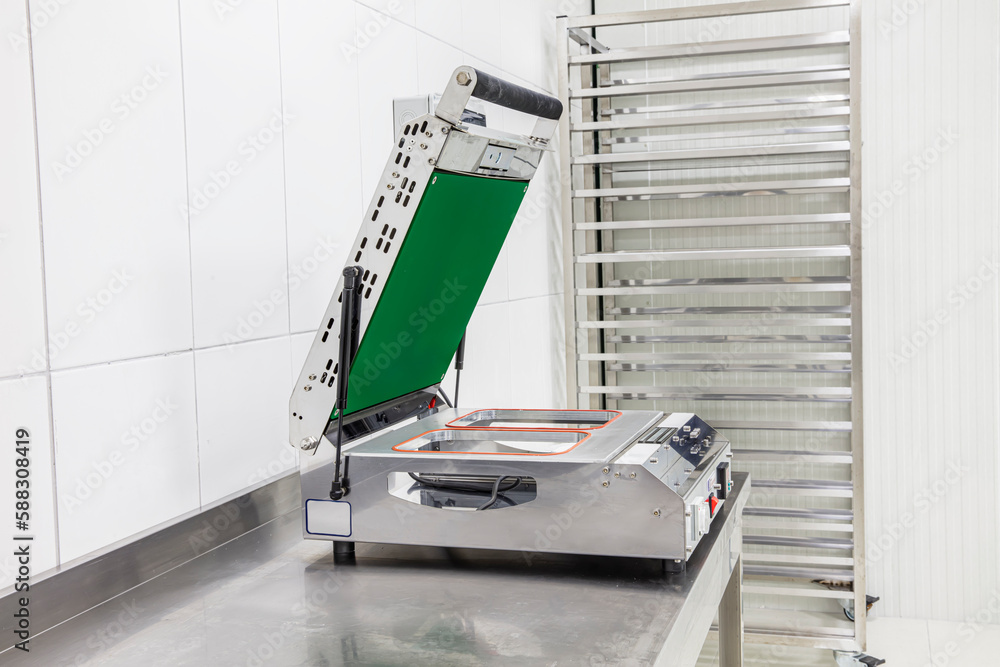 Cold room in warehouse with empty metal shelves. Food packaging machine on steel shelf in cold room. Refrigerator compartment in factory, store or restaurant Cold room in warehouse with empty metal shelves. Food packaging machine on steel shelf in cold room. Refrigerator compartment in factory, store or restaurant