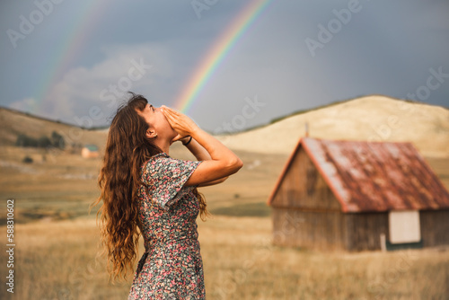 Optical illusion of rainbow coming out from mouth of woman standing in field photo