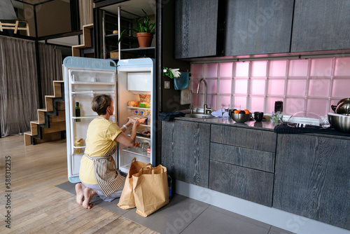 Woman stocking groceries in fridge at home photo