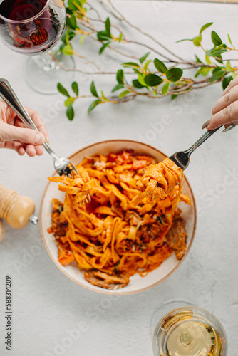 Italian pasta, tomato sauce. Two female hands in the frame, girls eat pasta, hold forks in their hands, top view, Italian cuisine.