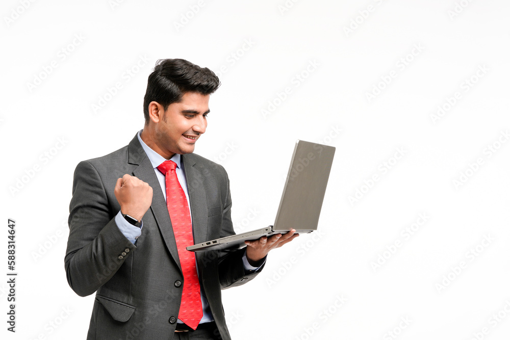 Young indian businessman in suit, holding laptop and giving a winning expression. Young indian businessman in suit, holding laptop and giving a winning expression.