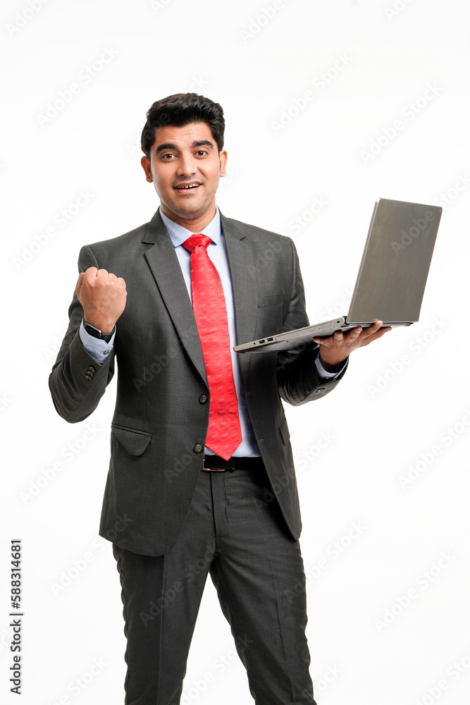 Young indian businessman in suit, holding laptop and giving a winning expression. Young indian businessman in suit, holding laptop and giving a winning expression.