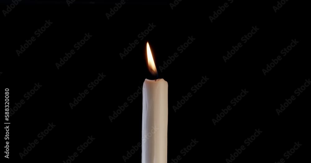A single white candle burning. Isolated candle slow motion burning with dark background. White paraffin candle with yellow shades burns on a black background. Slow motion. A single white candle burning. Isolated candle slow motion burning with dark background. White paraffin candle with yellow shades burns on a black background. Slow motion.
