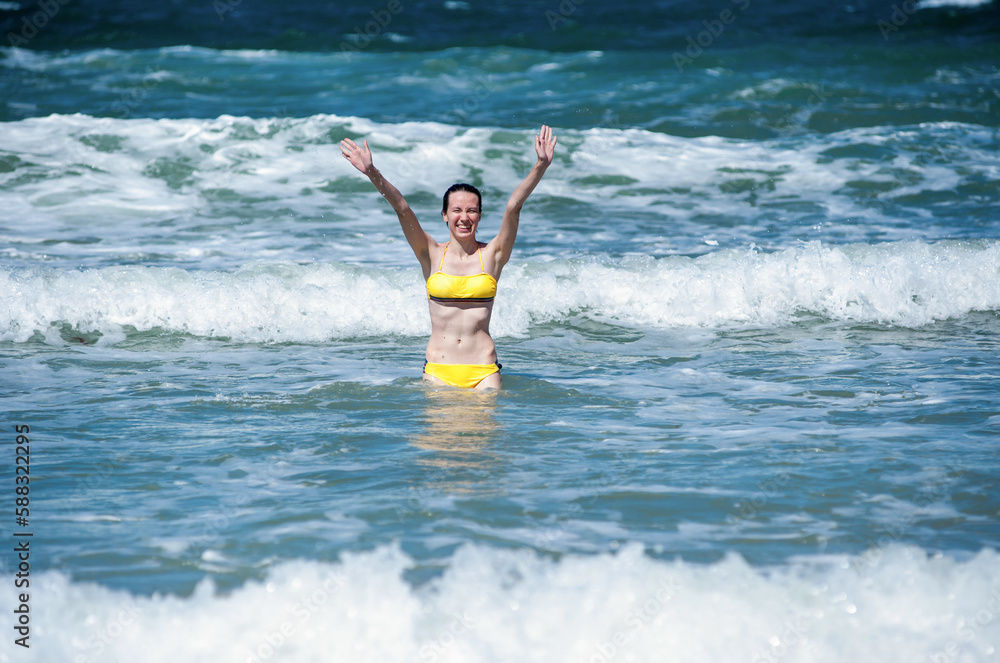 A woman in a swimsuit rejoices and has fun in the sea on the waves