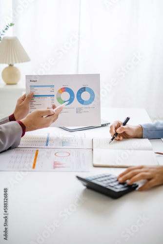 Two business people talking about report graph and analysis about finance budget or cost company and using calculator in office room.