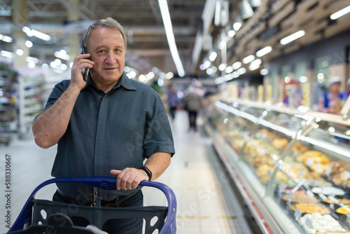 Elderly man consulting on mobile phone while shopping at grocery store photo