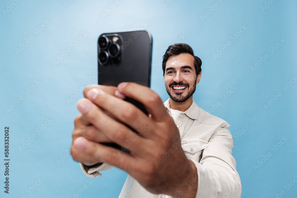 Portrait of a stylish man brunette smile with teeth and open mouth looking at the phone blogger with a beard taking selfies, on a blue background in a white T-shirt and jeans, copy space Portrait of a stylish man brunette smile with teeth and open mouth looking at the phone blogger with a beard taking selfies, on a blue background in a white T-shirt and jeans, copy space