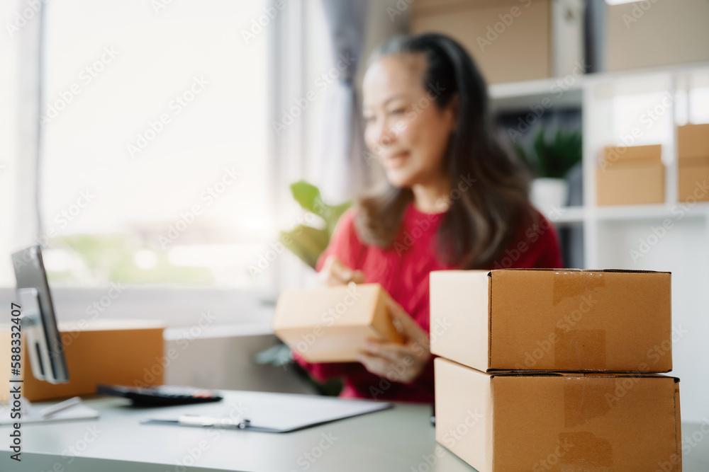 adult woman e-commerce business is writing a list of customers on paper before shipping to them, Concept of selling products online. adult woman e-commerce business is writing a list of customers on paper before shipping to them, Concept of selling products online.