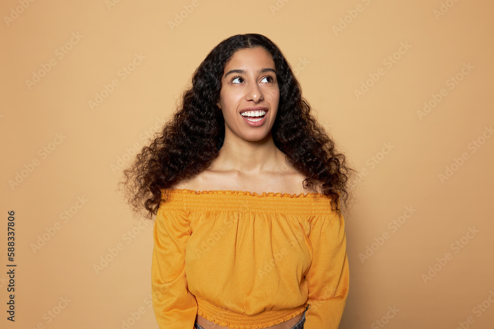 Portrait of happy excited joyful female with dark skin and long wavy hair standing against brown studio background looking up day dreaming, making wish, playing with her imagination Portrait of happy excited joyful female with dark skin and long wavy hair standing against brown studio background looking up day dreaming, making wish, playing with her imagination