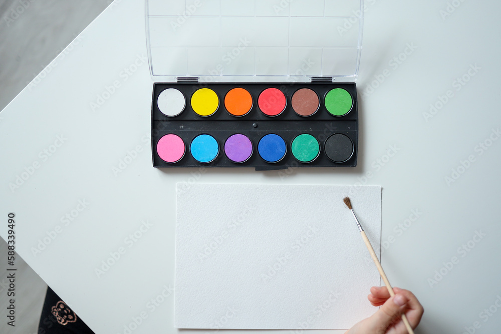 Little girl prepares to paint on a blank sheet of paper. Children's drawing. View from above Little girl prepares to paint on a blank sheet of paper. Children's drawing. View from above