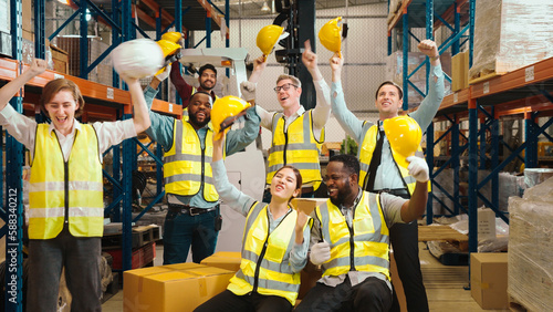 Multiracial warehouse workers in safety wear are dancing to relax after working hard on shipping goods. Male and female logistic employees are spending time together to celebrate the success of jobs.