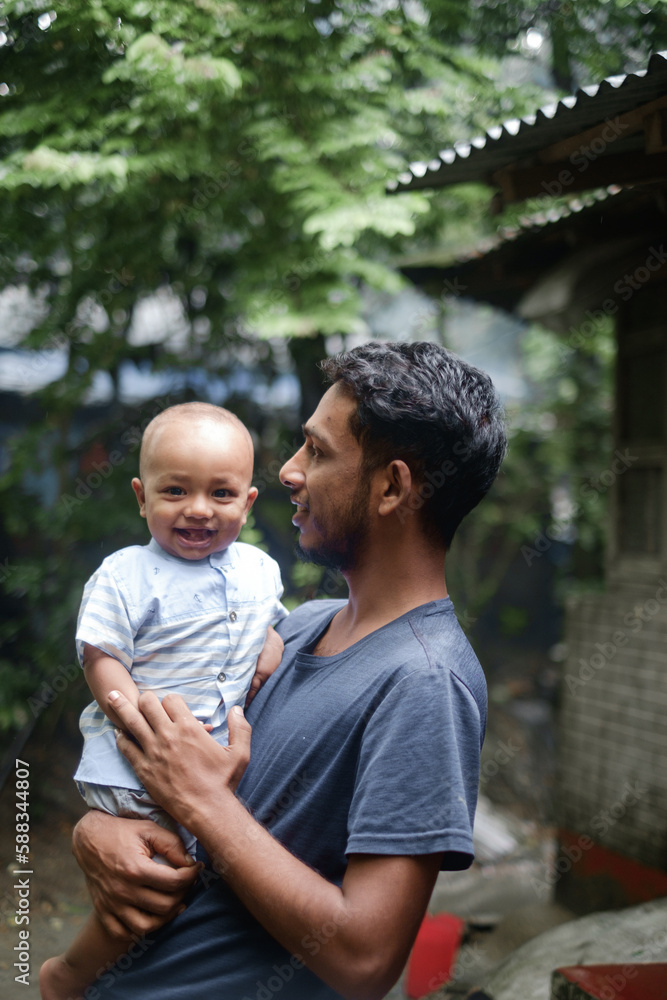 Fototapeta premium South asian young rural father holding his little son, village baby boy playing with his young dad, lovely family moments in outdoor 