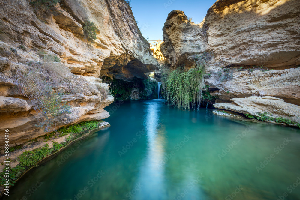 Beautiful surroundings of a waterfall called Salto del Usero in Bullas, Murcia, Spain. Blue and crystalline waters under a yellow rock cave