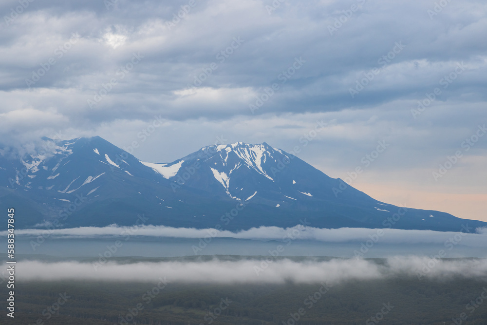 Beautiful evening landscape. View of the volcanoes. Overcast weather. Low clouds. Nature of the Kamchatka Peninsula. Travel and tourism in Siberia and the Russian Far East. Kamchatka Territory, Russia