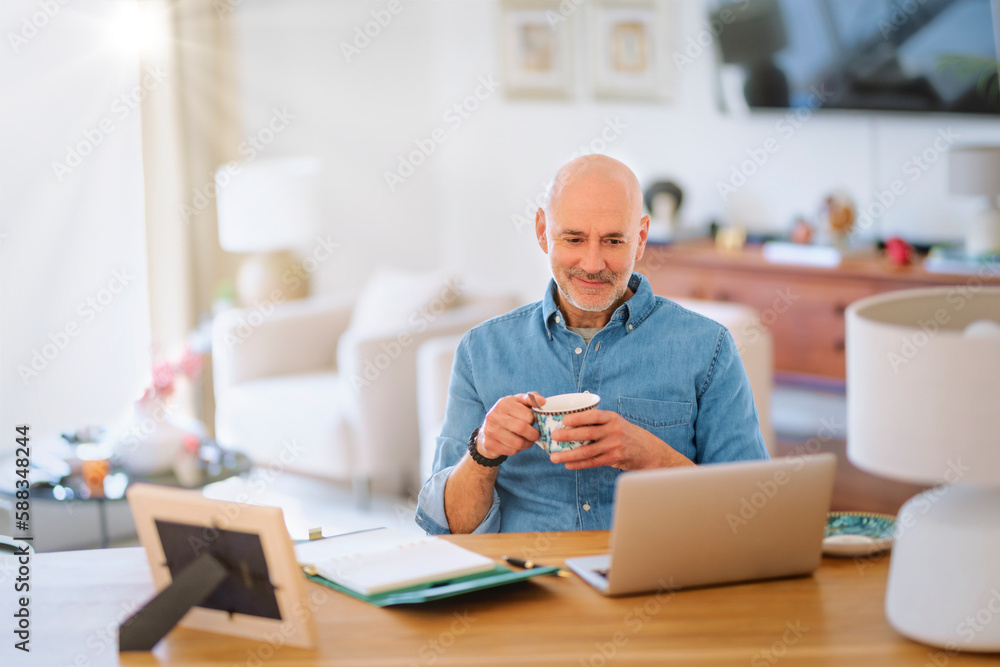 Mid aged man wearing casual clothes and using laptop for work while sitting at home Mid aged man wearing casual clothes and using laptop for work while sitting at home