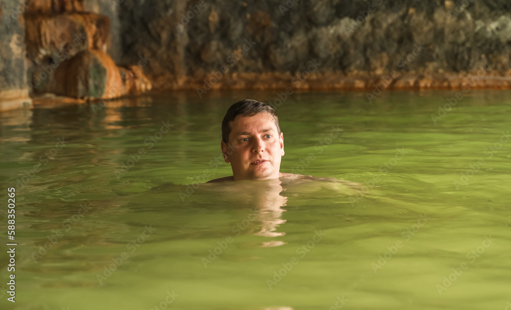 Man bathe swim in outdoor cave, dirty hot springs. Thermal water bath pool. Healthy natural clay. Yellow green mud. Spa wellness procedures, relax. Family winter vacation in mountain hotel