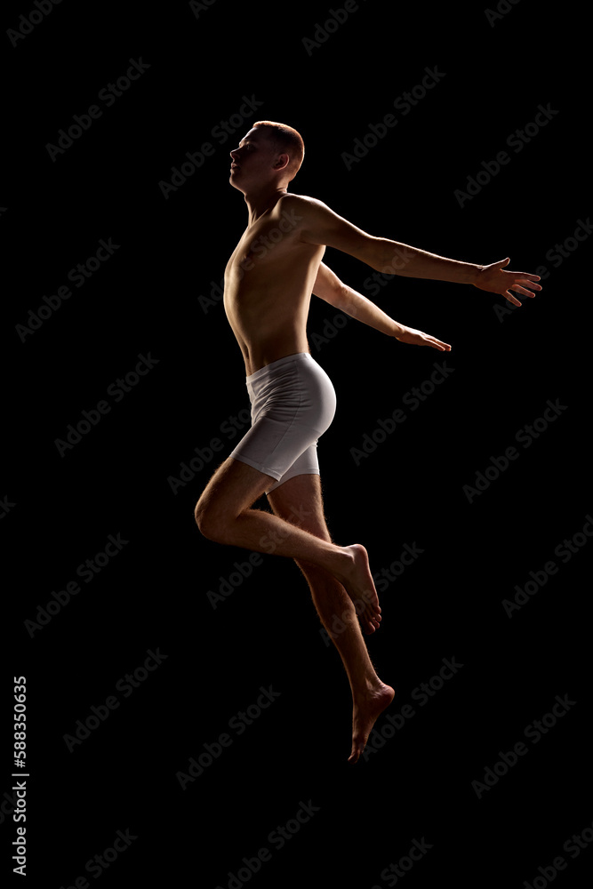 Portrait of young good-looking redhead man wearing underwear and jumping with open hands over dark background