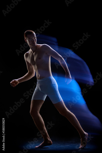Photo of young handsome male body glowing neon light over dark background. Mixed neon light