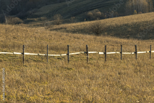 Old wooden fence on yellow rural field in countryside in autumn nearby hill when sun goes down