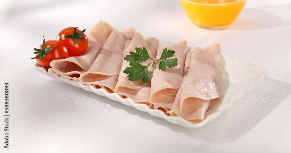 ham on a plate. meat delicacy with cherry tomato on a light background. turkey ham slices with parsley. cold appetizer on a white tablecloth. treat close-up. ham on a plate. meat delicacy with cherry tomato on a light background. turkey ham slices with parsley. cold appetizer on a white tablecloth. treat close-up.