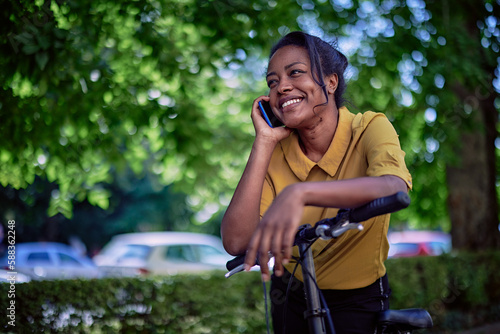 Smiling young woman talking on the phone while taking a break from cycling in a city park.