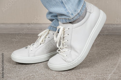 Women's white leather sneakers on the legs indoors. Shoe care. Shoe laces and lacing