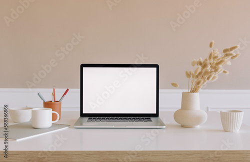 Modern workplace mockup with open laptop computer, dried flowers in vase , stationery on the table. Minimal style. Copy space. Business, marketing, portfolio showcase mockup.