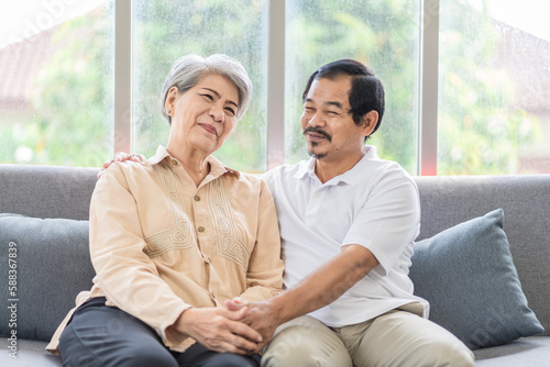 Asian couple, elderly man and woman sitting on the sofa having fun chatting together at home. Concept: health insurance, life insurance, retirement happiness.