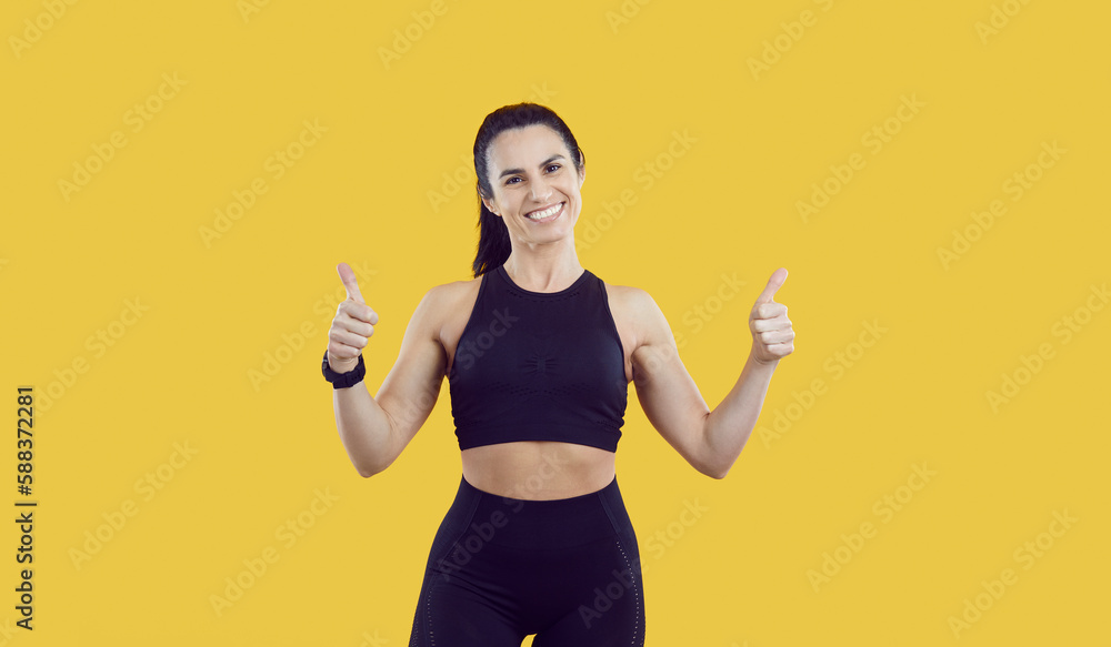 Portrait of smiling toned female athlete in sportswear isolated on yellow studio background show thumbs up. Active overjoyed young woman coach or trainer recommend sport and physical activity. Portrait of smiling toned female athlete in sportswear isolated on yellow studio background show thumbs up. Active overjoyed young woman coach or trainer recommend sport and physical activity.