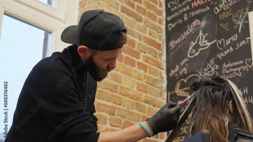Male hairdresser applying hair dye to female client hair using a brush in a beauty salon. Hair highlighting process. Low-angle view. High quality 4k footage