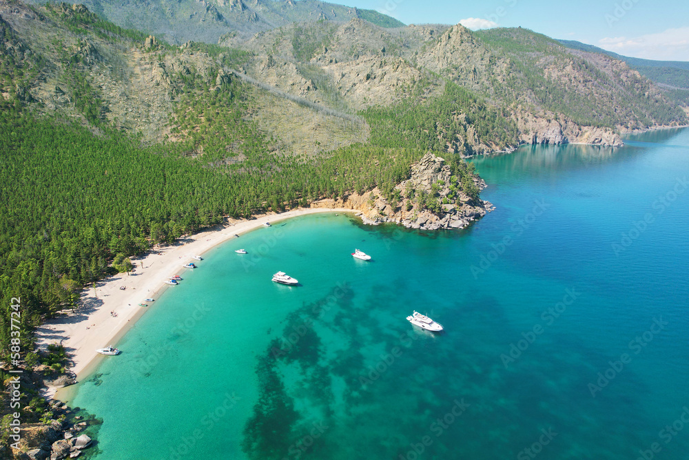 Yachts near the shore of Lake Baikal, in Babushka Bay, tourists sunbathe on a sandy beach. Beautiful summer seascape. Aerial view