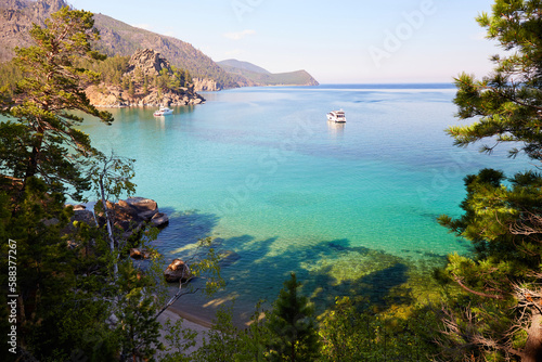 Picturesque summer landscape of Lake Baikal. Yachts in Babushka Bay, turquoise water color. Coniferous forest. Recreation and travel in the wild.