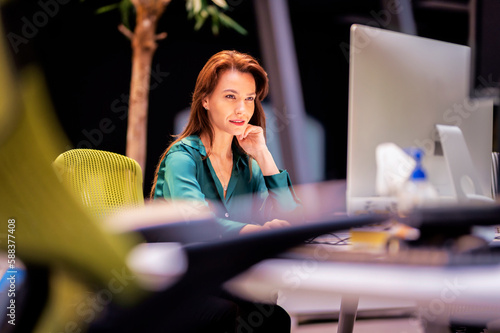 Confdient professional woman sitting at desk and surrounded by computers while working at the office photo