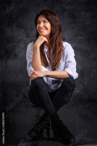 Studio portrait of a brunette haired attractive woman wearing white shirt and black jeans while posing at isolated dark background