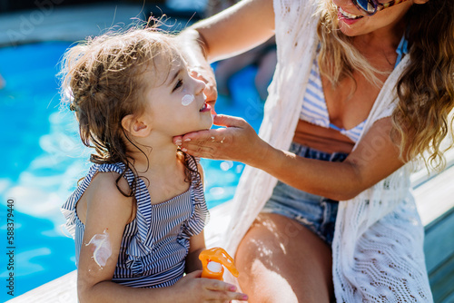 Young mother applying sunscreen lotion to her daughter. Safety sunbathing in hot day. photo