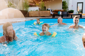 Multi generation family having fun and enjoying swimming in backyard pool during summer holiday.