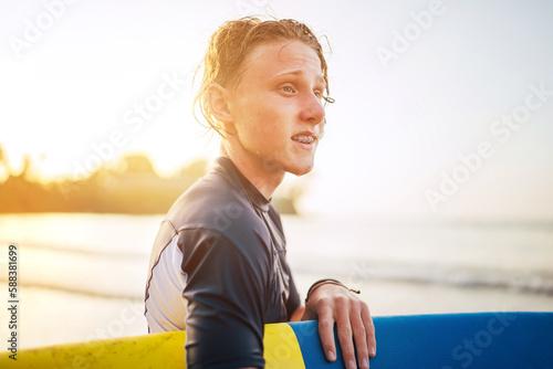 Portrait of a teen boy with Dental braces and wet hair with a surfboard goes for surfing. He is smiling and walking into the water. Happy boyhood and active vacation time concept