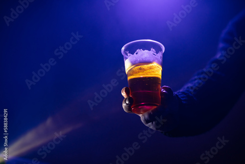 Person holding a plastic cup of beer in the nightclub.