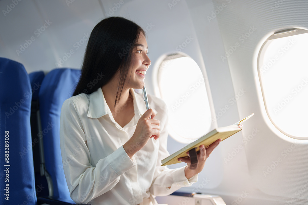Asian business woman passenger sitting on business class luxury plane while working using notebook book while travel concept Asian business woman passenger sitting on business class luxury plane while working using notebook book while travel concept