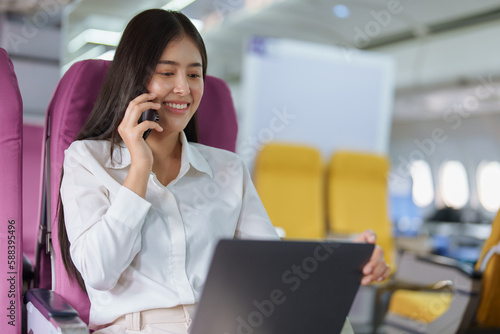 Asian business woman passenger sitting on business class luxury plane while working using smart phone mobile talking or video conference and travel concept