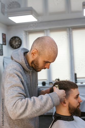 A hairdresser or barber is working with a shaving machine on the hair.