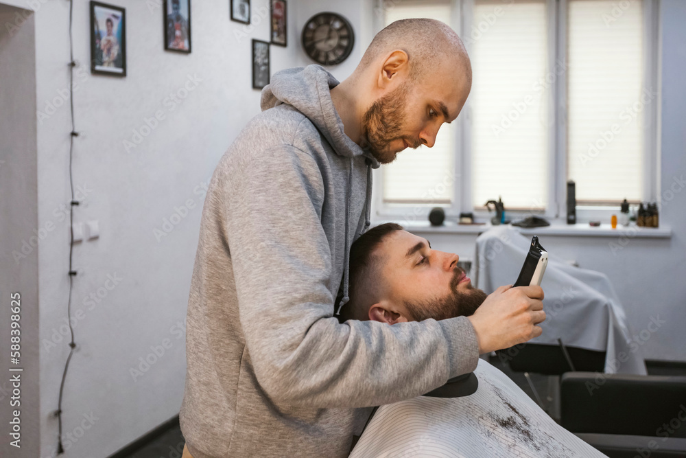 A barber is working on a client's beard.