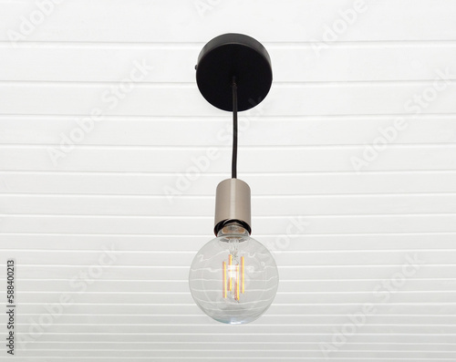 A lamp made with a tuned off light bulb. Chandelier in vintage style hanging on white wooden slatted ceiling. Lighting and Electricity.