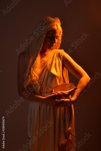 portrait of beautiful blonde woman wearing a fantasy goddess toga costume with crystal crown. Backlit a glowing isolated studio background with orange silhouette lighting.