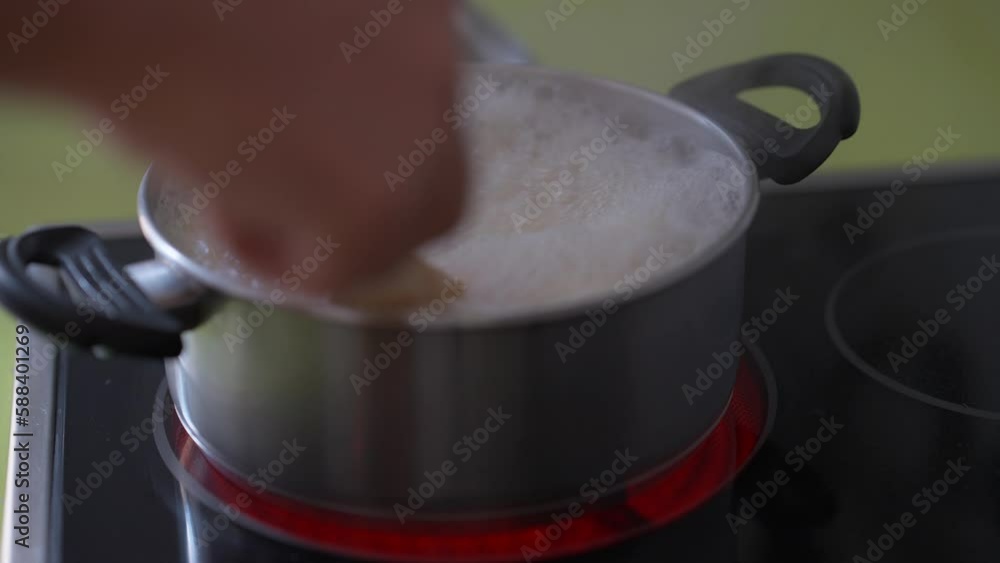 Close-up cooking pot with boiling water bubbling and male Caucasian hand stirring dumplings. Unrecognizable man cooking dinner at home in kitchen Close-up cooking pot with boiling water bubbling and male Caucasian hand stirring dumplings. Unrecognizable man cooking dinner at home in kitchen