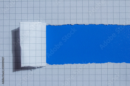 Graph paper torn on a blue background. Ripped checkered paper with copy space.