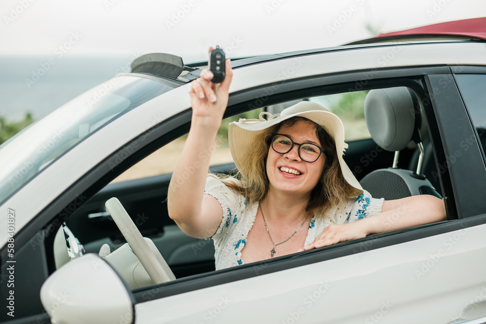 Travelling woman holding keys to new car and smiling at camera - ownership and purchase automobile concept