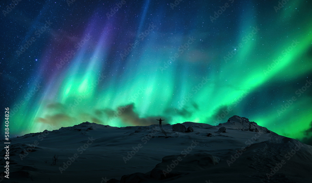 Aurora borealis over silhouette cheerful man on top of mountain in arctic circle at Norway