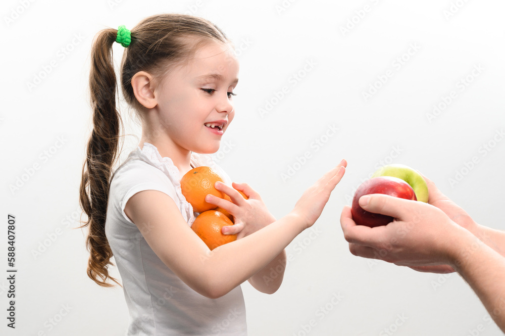 Portrait of a small beautiful girl on a white background with tangerines in her hands, who is also offered apples. Portrait of a small beautiful girl on a white background with tangerines in her hands, who is also offered apples.